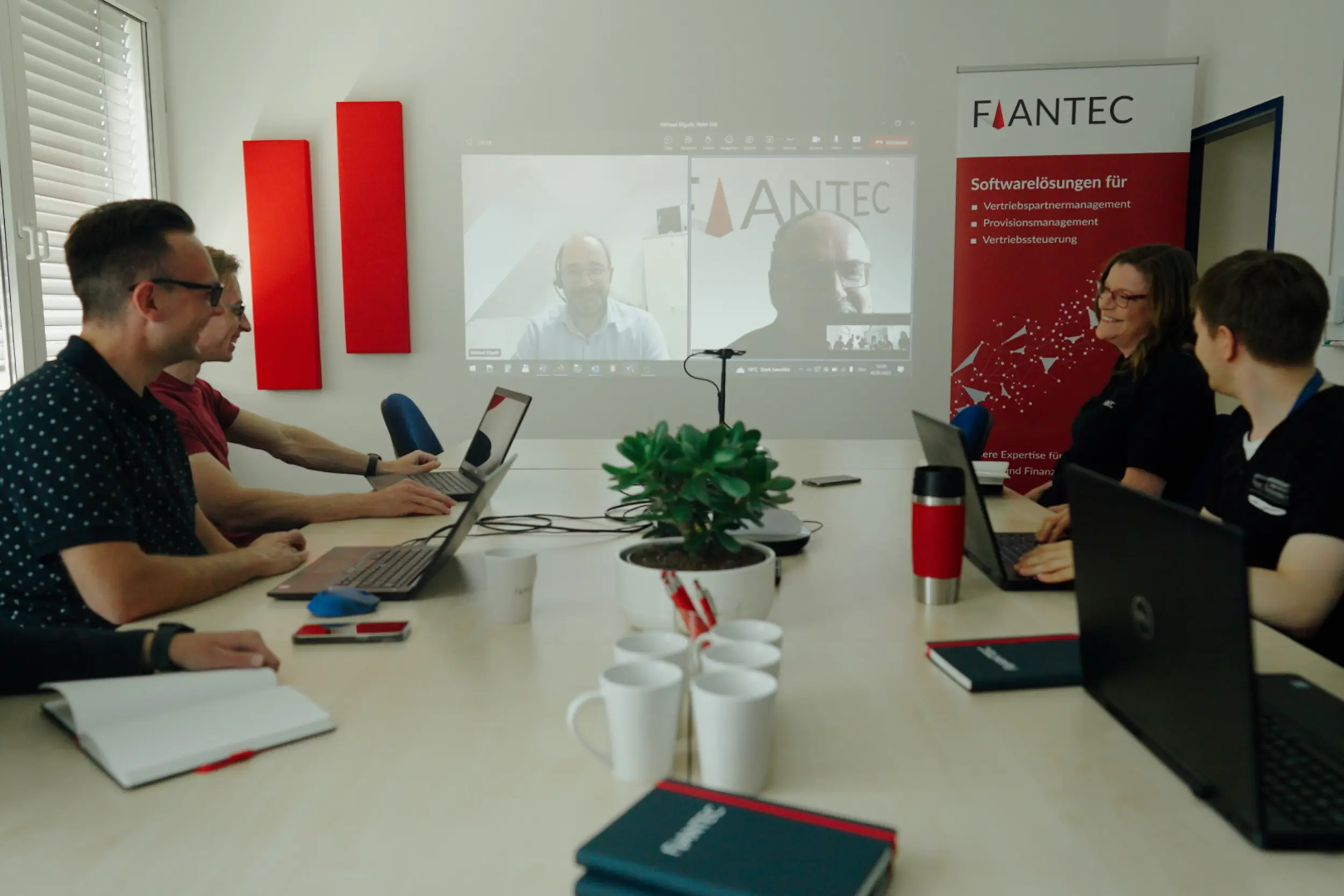 Team Mitglieder von FiANTEC unterhalten sich in einem Besprechungsraum während eines Online-Meetings